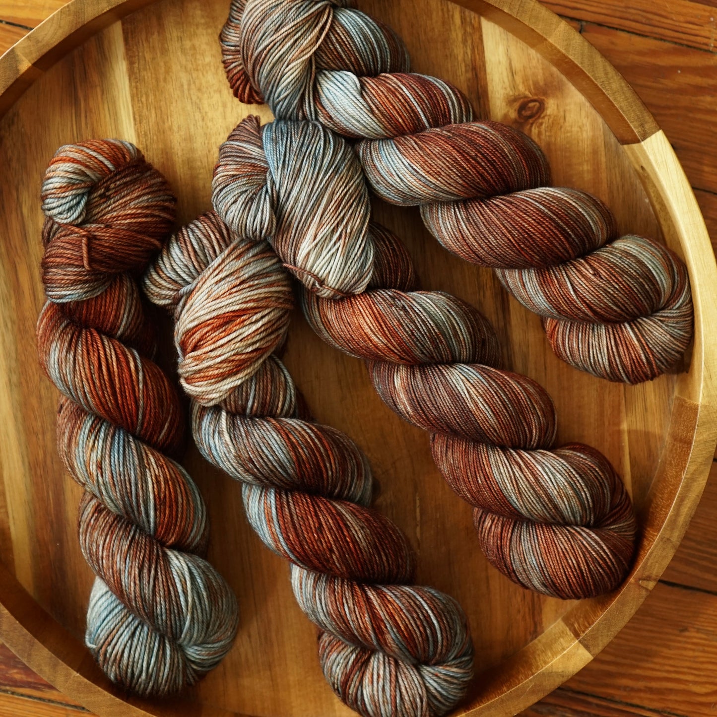 Skeins of multicolored, red teal and brown yarn arranged on a round wooden tray.