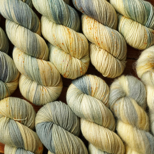 Multicolored pastel yellow and teal grey skeins of yarn in a variety of fiber blends arranged artfully at a slant on a wooden surface.