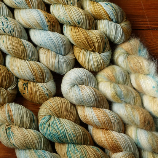 Multicolored golden yellow and sky blue skeins of yarn in a variety of fiber blends arranged artfully on a wooden surface.