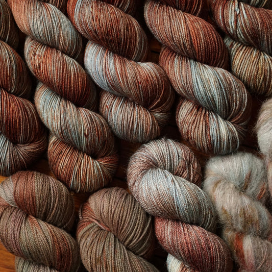 Close-up of skeins of red, brown and teal yarn with earthy tones in a variety of fiber blends.