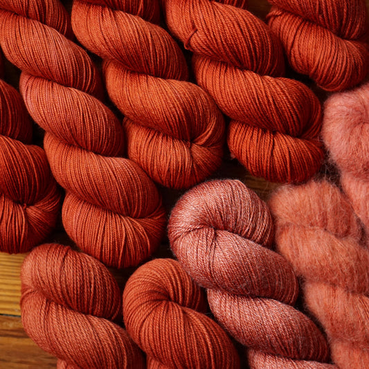 Close-up of red yarn skeins in a variety of fiber blends on a wooden surface