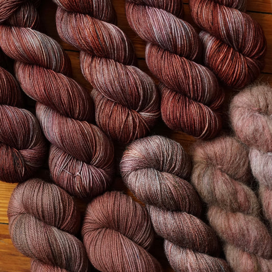 Skeins of reddish brown and teal gray yarn on a wooden surface