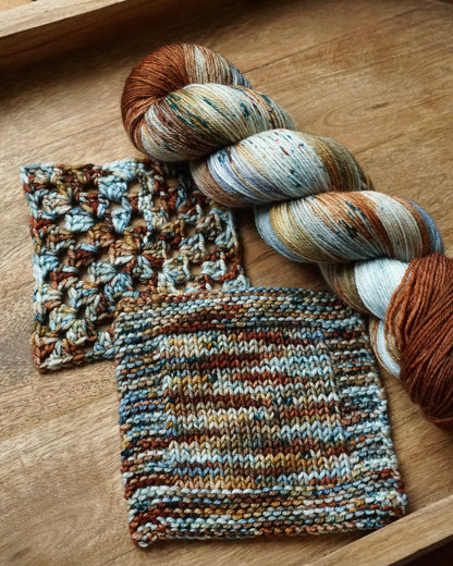 Knitted swatches and skein of yarn on a wooden tray